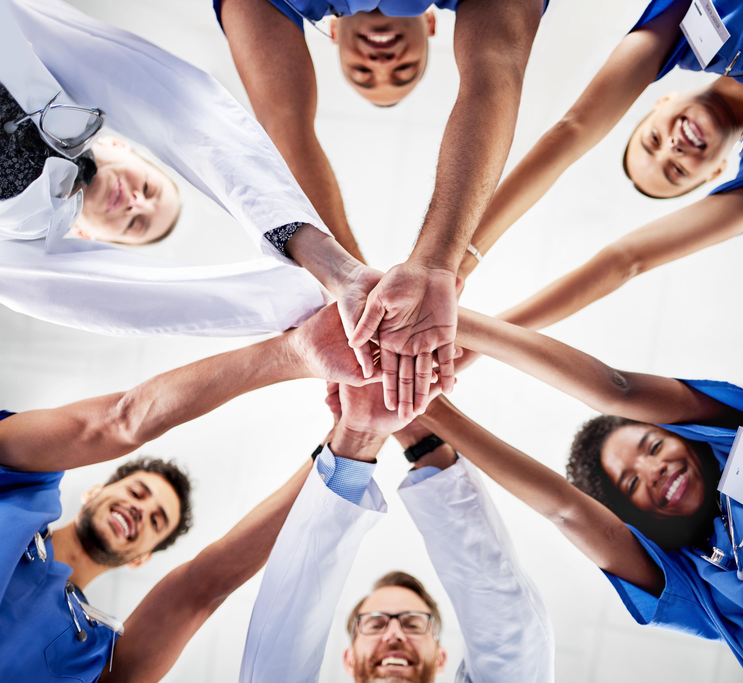 A team of healthcare professionals standing in a circle with their arms extended into the centre
