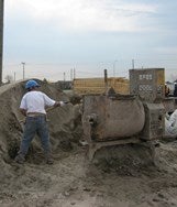 A person shoveling sand repeatedly into the mixer