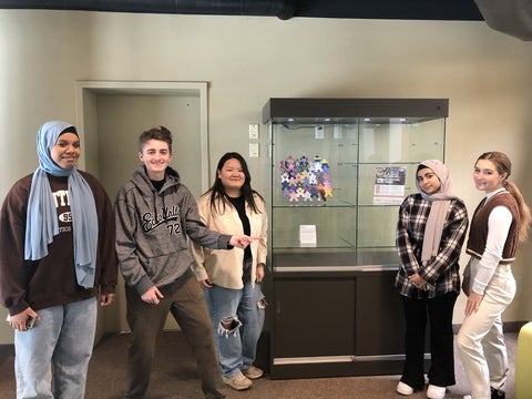 5 high school students who received the Peace Innovators scholarship standing in front of a display case