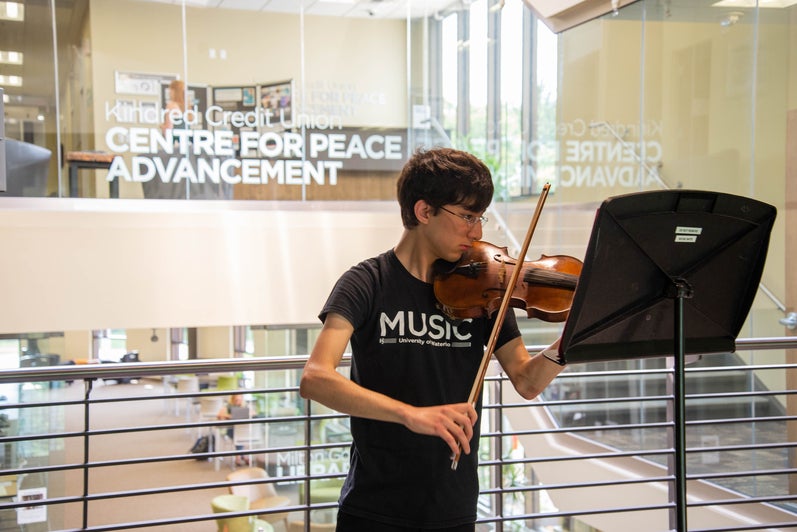 Grebel music student playing the violin outside the CPA floor