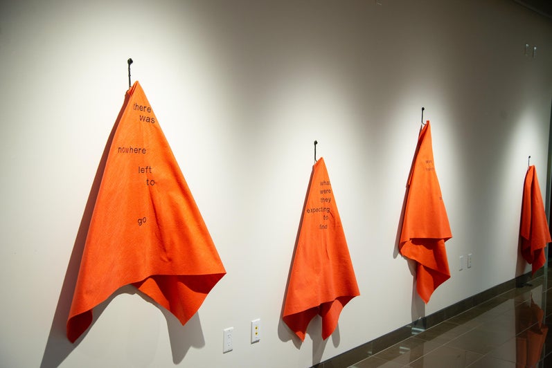Four orange blankets hanging on the wall in the Grebel Gallery