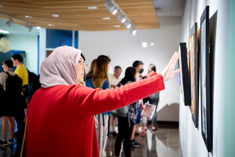 A woman in a red coat points at a picture on the wall of the Grebel Gallery