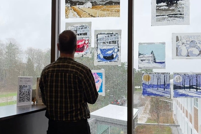 Man in silhouette looking at the rice paper batiks on the window against a rainy sky