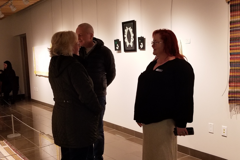 three people talking in front of art pieces on a wall