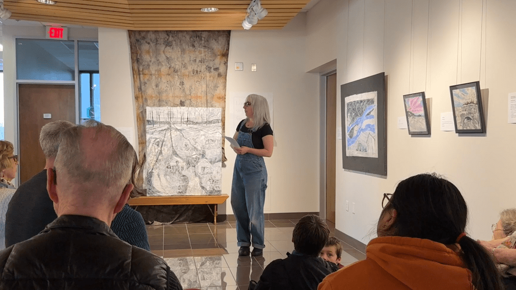 woman speaking to an audience in a gallery
