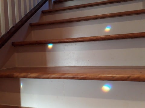 Small rainbows created by a prism shining on wooden stairs