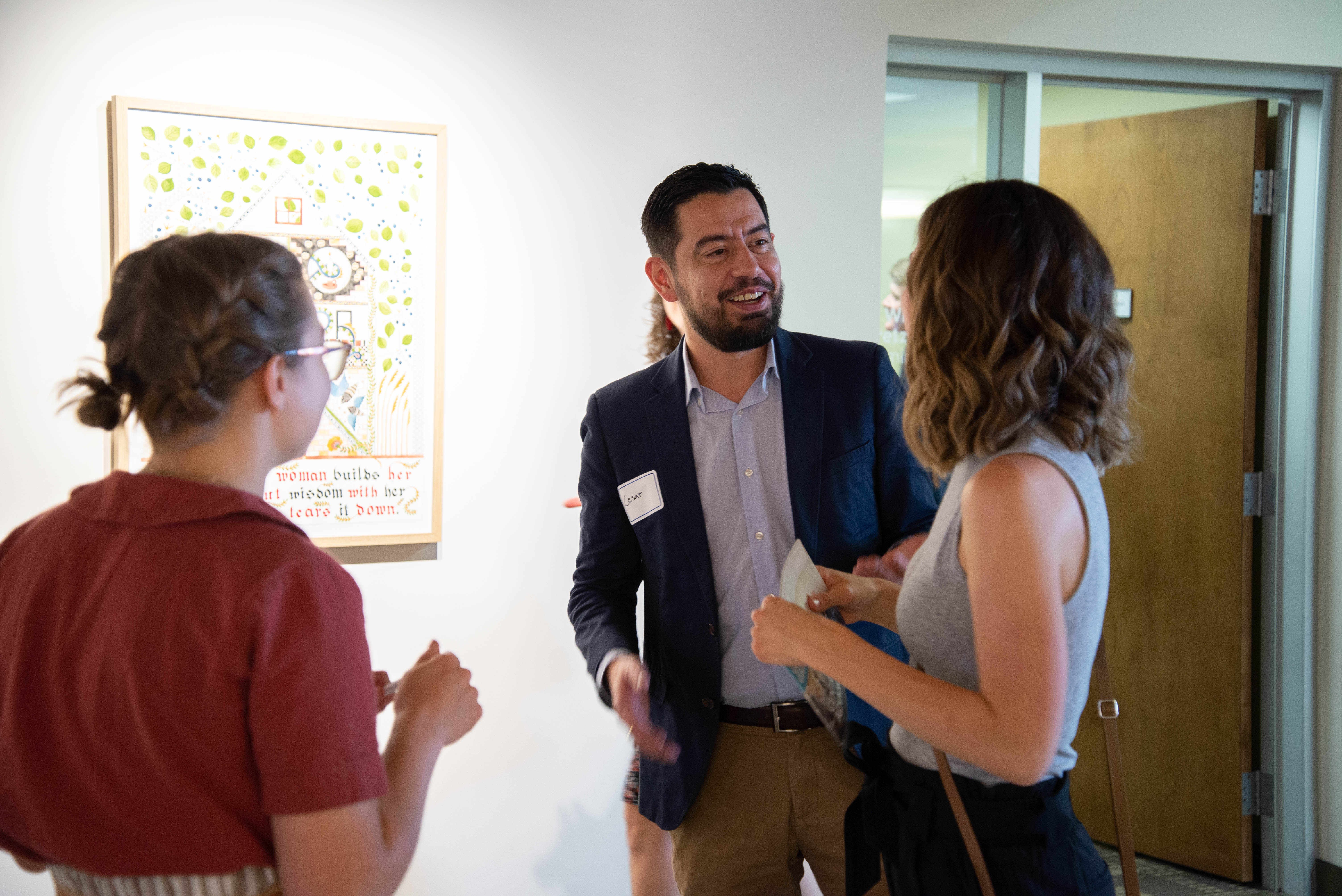 Three people talking in front of a painting in the Grebel Gallery