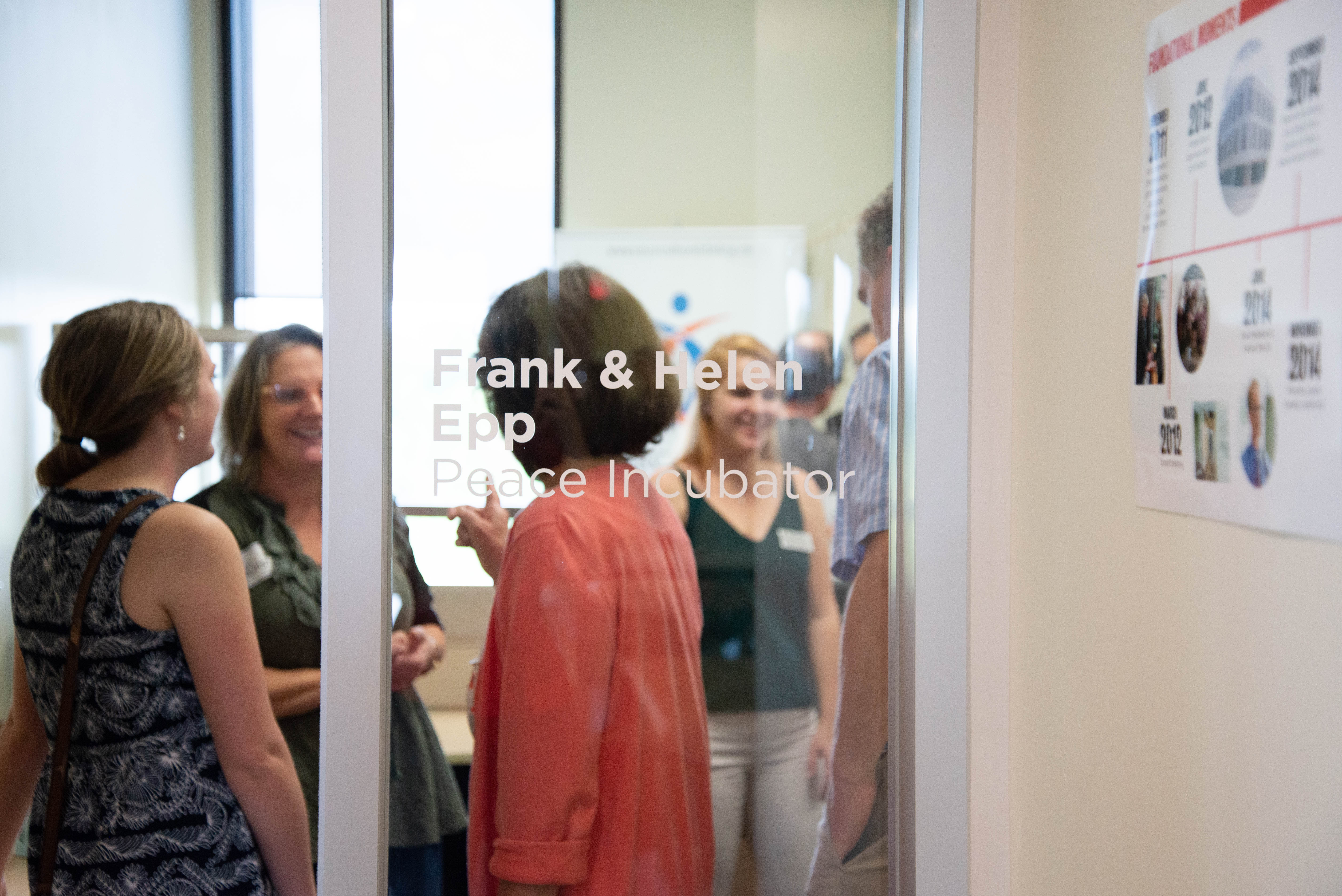 A group of people standing on the other side of the glass wall of the Frank and Helen Epp Peace Incubator