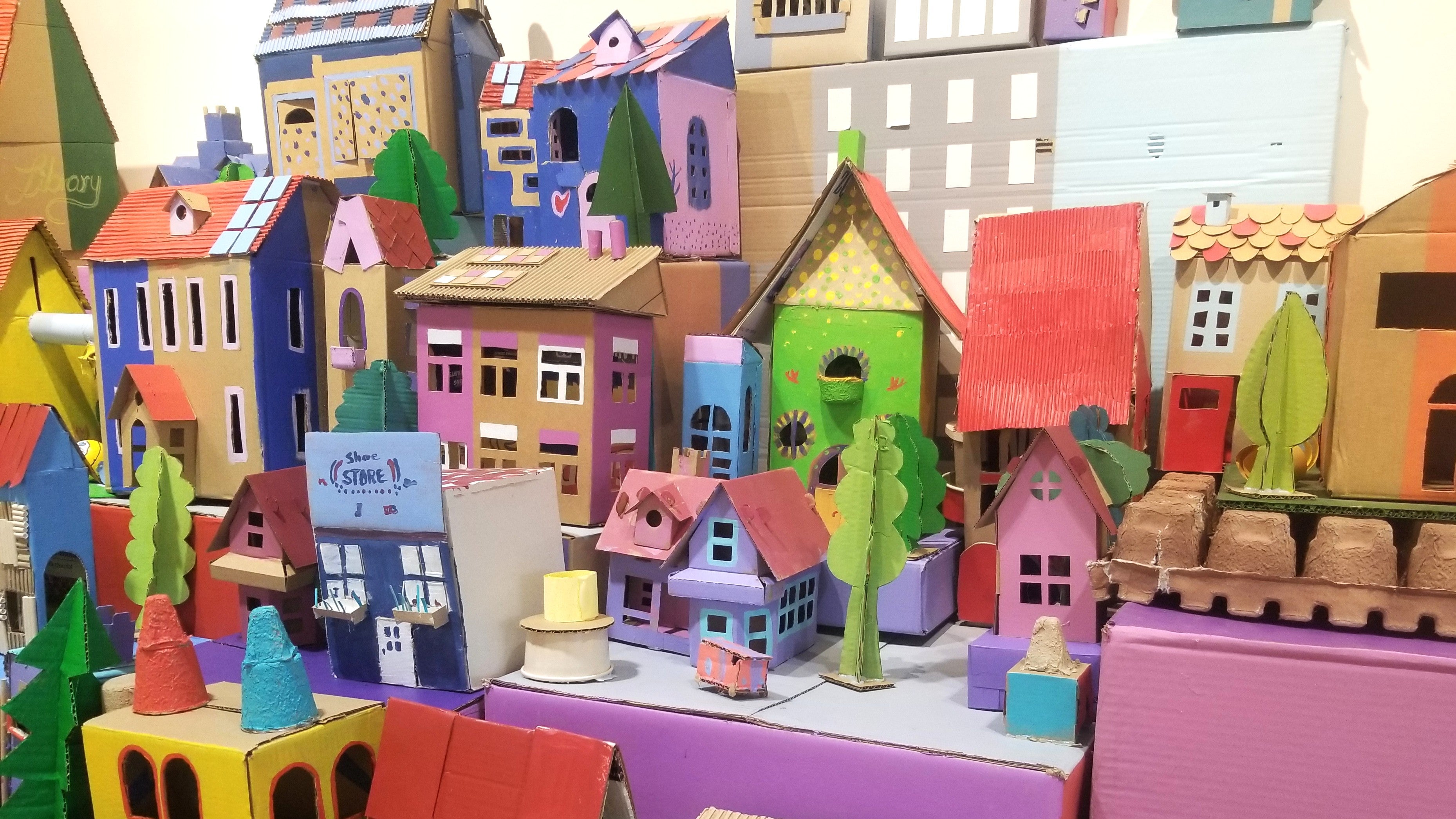Houses made of colorfully painted cardboard pile into a joyful envisioned city