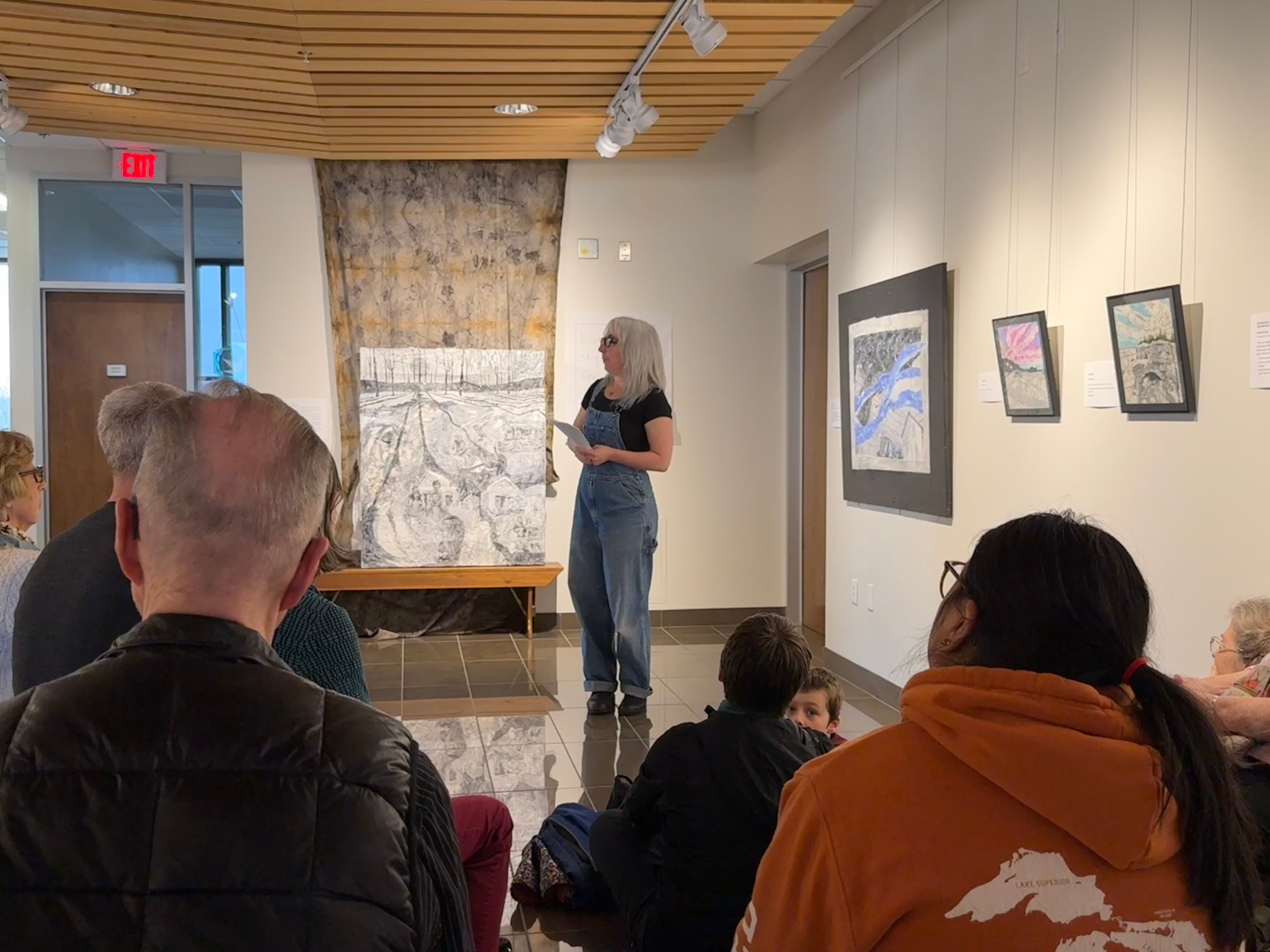 woman speaking to an audience in a gallery