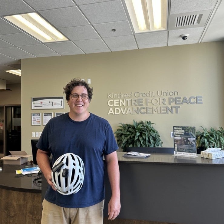 Sean smiling in front of the cps sign while holding a bike helmet