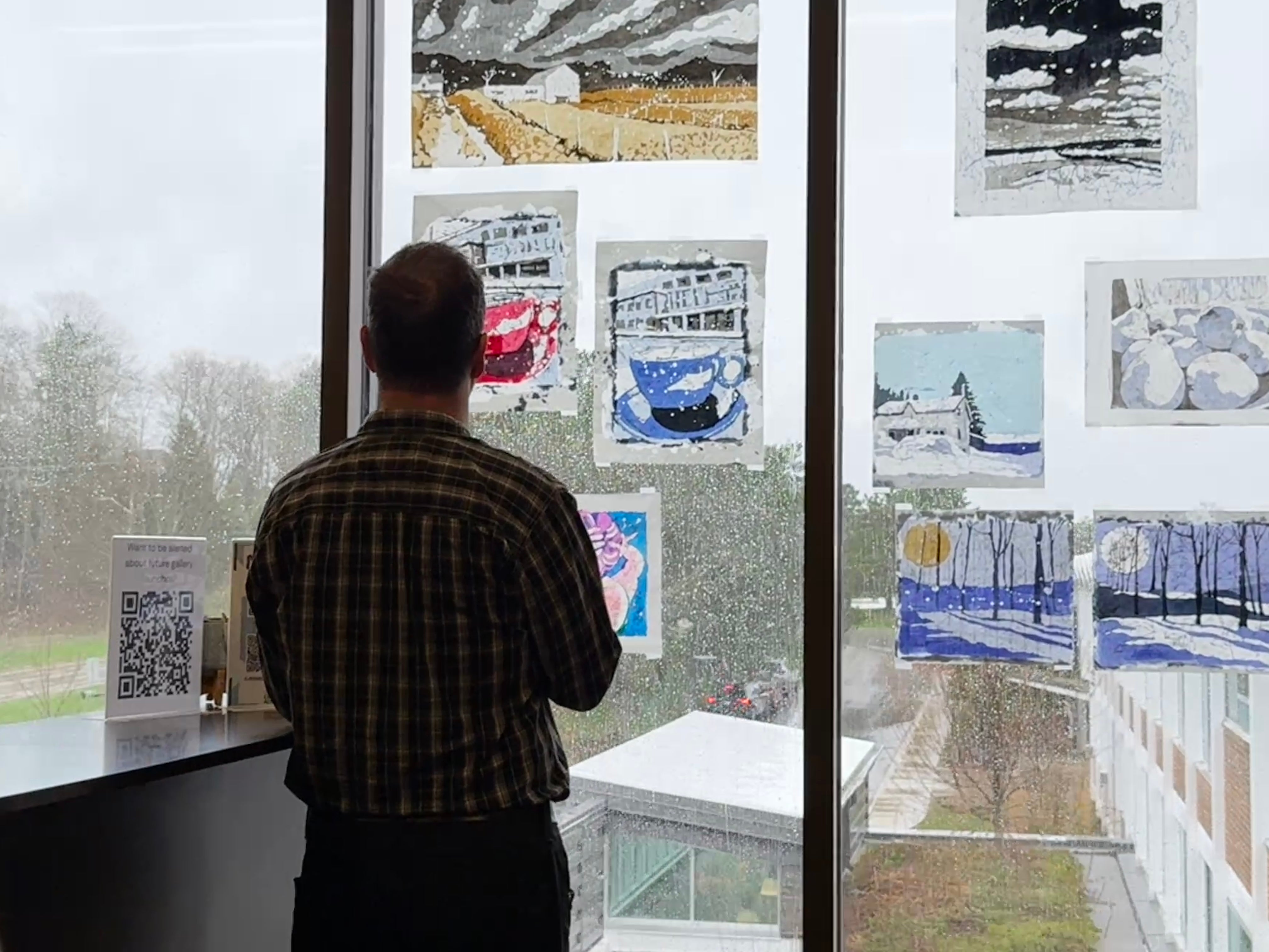 Man in silhouette looking at the rice paper batiks on the window against a rainy sky