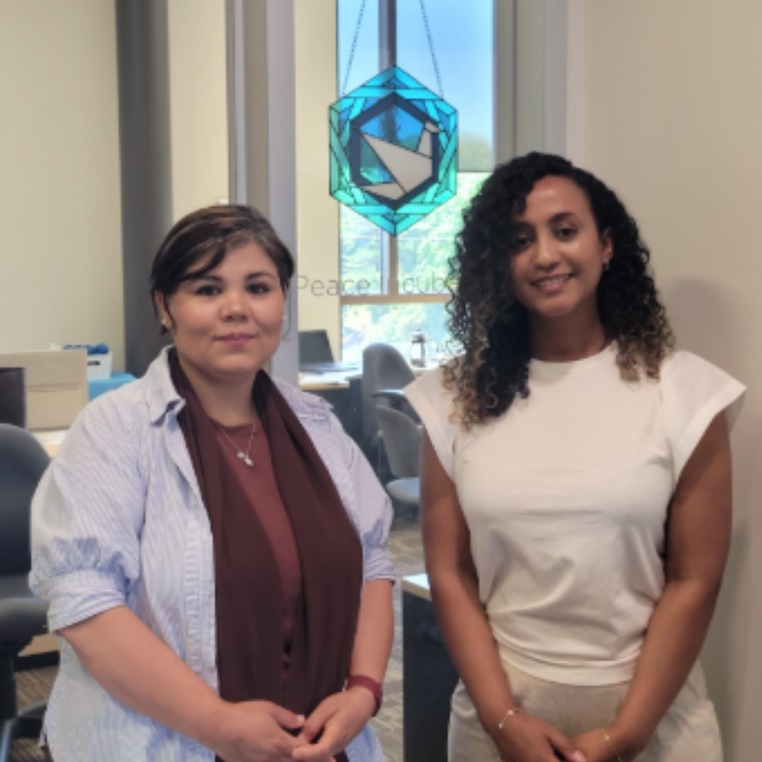 Wazhma and Addi stand in front of the Grebel Peace Incubator dove stained glass window
