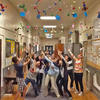 a large group of students in a school hallway reaching up to the atom model decorations hanging above