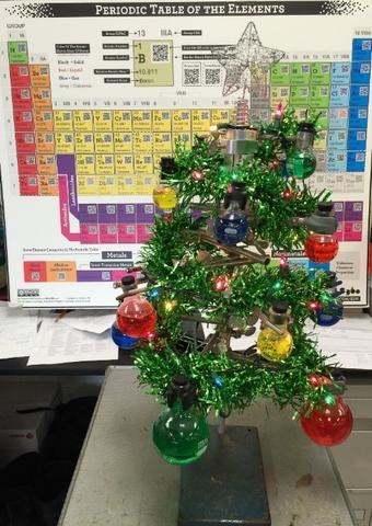 Christmas tree with flasks filled with coloured liquid, periodic table in background.