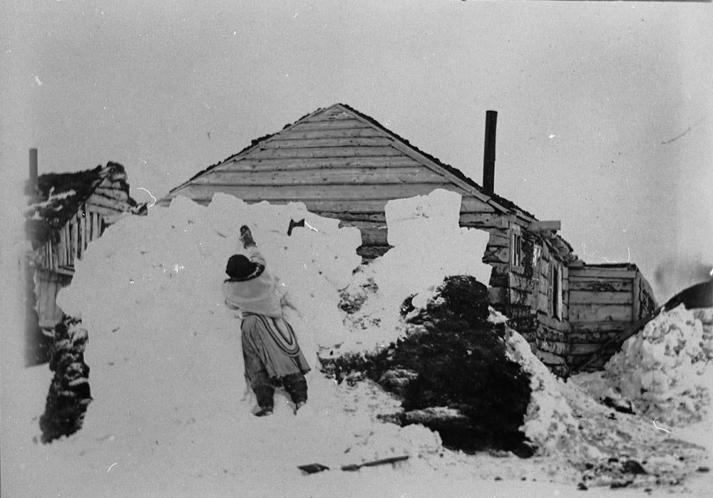 An Inuit woman packing snow blocks around her house to help insulate.