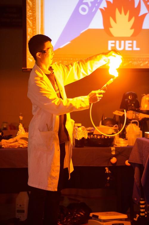 Micheal Ng doing a demonstration with a long tube and a large golden flame produced at its end