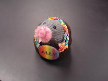 A mole made out of yarn wearing a beaded necklace and wearing a name tag with Ally written on it