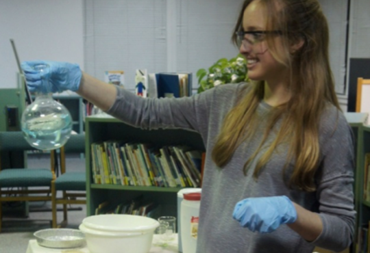 a girl swirling a round bottom flask with a blue solution 