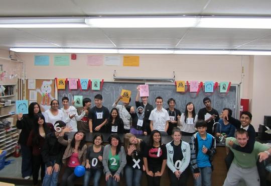 Students in a classroom with many wearing numbers on their T-shirt that combines to form 6.02 x 1023 Avogadro's number.