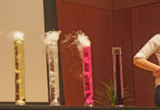 girl looking at five colourful graduated cylinders with smoke coming out of each