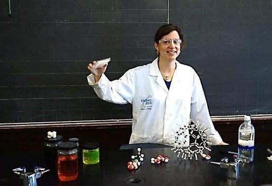 Jennifer Pitt-Lainsbury in a lab coat holding up a model 