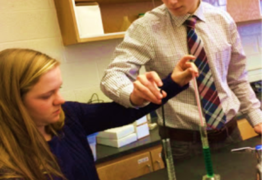 Students putting a straw into a graduated cylinder.