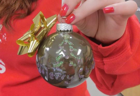 Girl holding up Christmas tree ornament.
