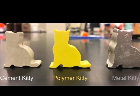 three molded cats of the same shape – one in gray cover cement, one yellow polymer and one silver metal
