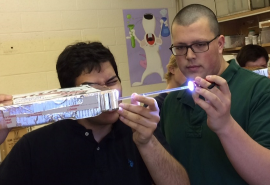 Students with lighted rods in cardboard boxes.