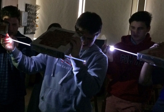 Students with lighted rods in cardboard boxes.