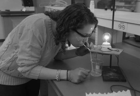 girl blowing into a solution in a beaker and a light bulb lighting up