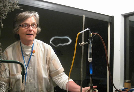 A teacher in front of a classroom looks on with amazement as a smoke ring is produced in a reaction demonstration  