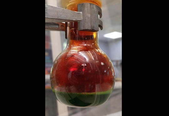 a round bottom flask with green solution and a brown gas coming from inside