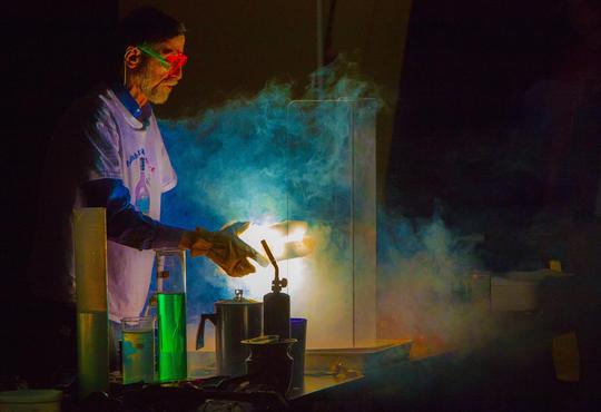 Lee Marek doing a demo in a darken room – he has large gloves and is holding a block of dry ice that is glowing