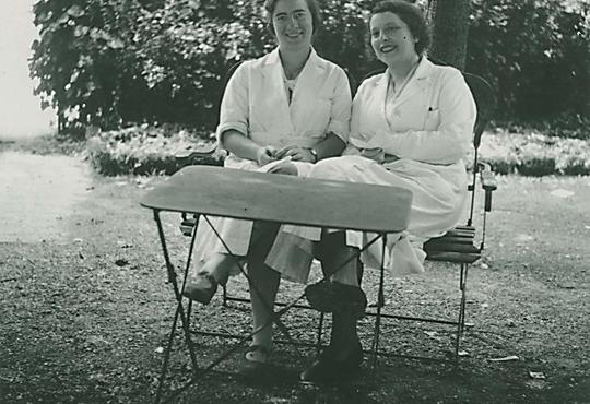 Marguerite Perey and Madam Curie smiling at outdoor bench.
