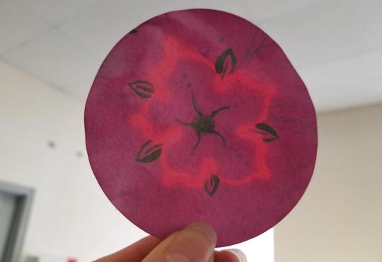 a hand holding a reddish paper circle with a light pink and green flower design