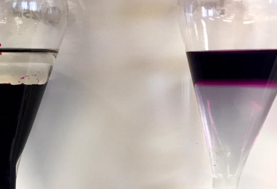 Two separatory funnels side-by-side both having two layers – clear layer atop a dark purple solution; purple layer atop clear 