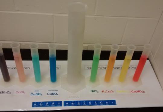 8 graduated cylinders with different colourful solutions with one large cylinder in the middle to look like a menorah 