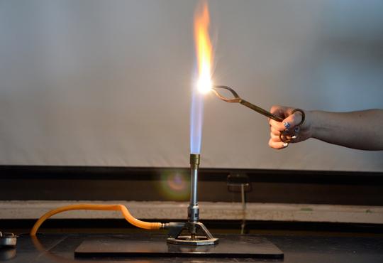 Bunsen burner and burning substance held in the flame by tongs.