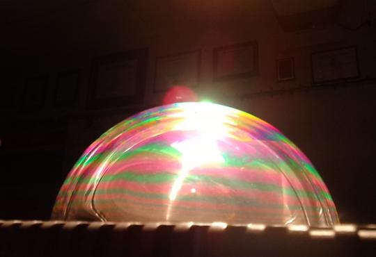 Large soap bubble with colourful refracted light on surface.