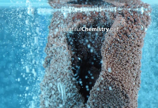 a blue solution with a brownish metal covered in bubbles on the surface and in solution 