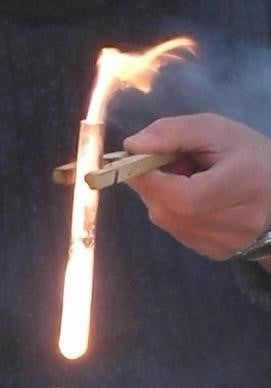 Hand holding clothespin holding test tube containing flame.