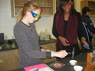 Two girls performing ethanol combustion reaction. One is holding a test tube over the reaction.