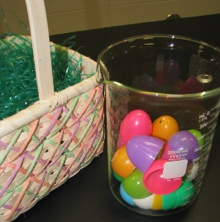 Colourful plastic Easter eggs opened in half in a beaker next to a basket.