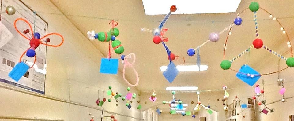 Handmade molecule shapes hung on suspended line in school hallway.