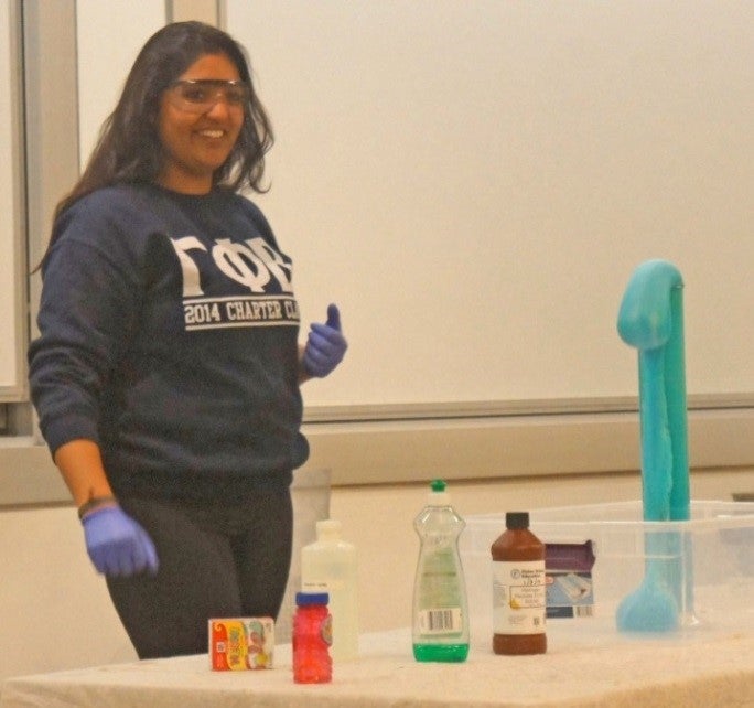 Girl standing behind table containing chemistry demonstration.