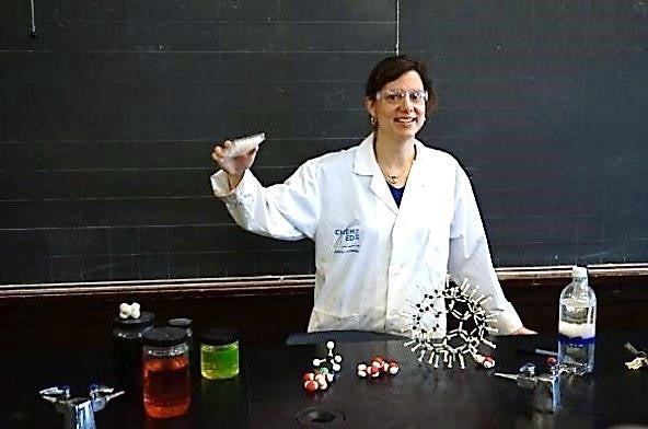 Teacher behind table containing various chemistry classroom objects.