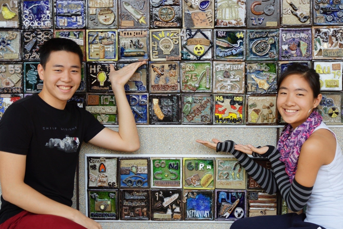 Boy and girl posing in front of handmade periodic table.