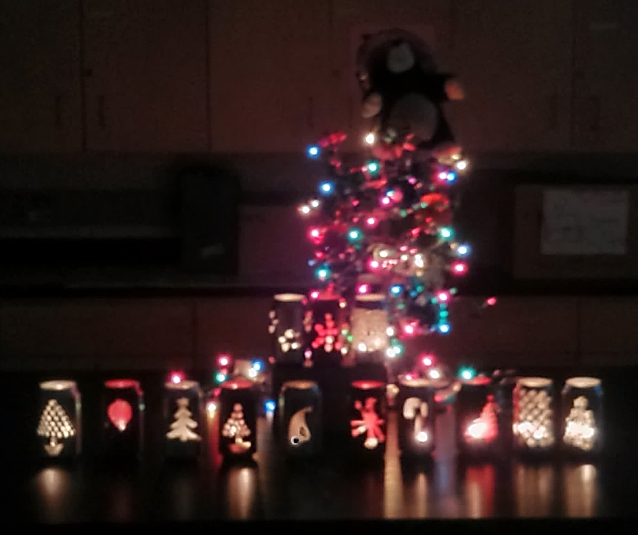Pop can candleholders placed in front of small Christmas tree.